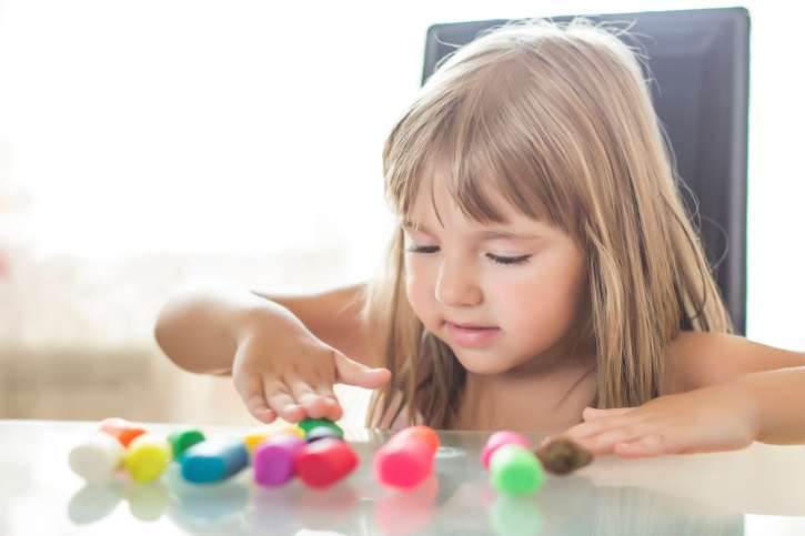 A young girl playing alone with colored clay
