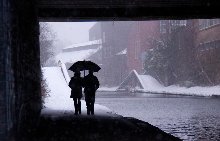 Couple walks out from under bridge into snow with shared umbrella