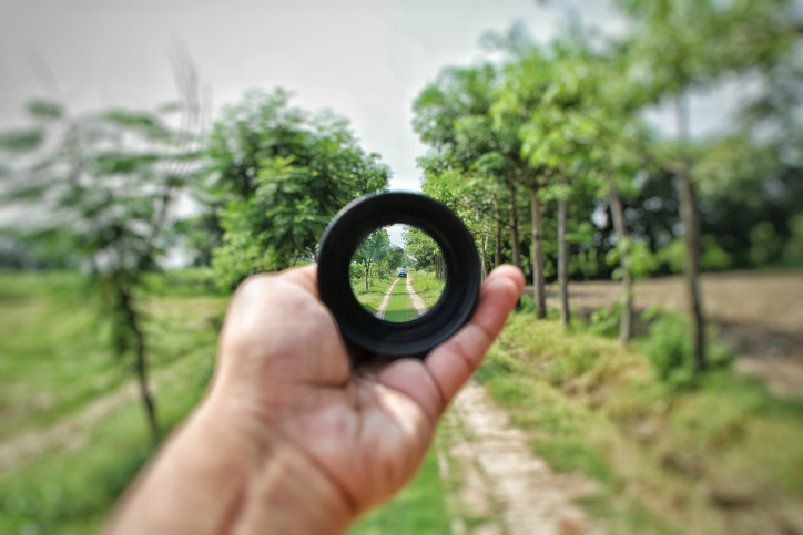 Outstretched hand holds lens that shows clear focus of tree-lined road