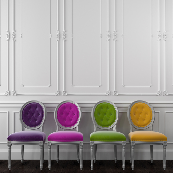 Four colorful empty chairs lined up against a white wall