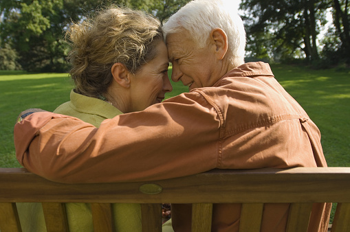 Older couple on bench smiling with heads together