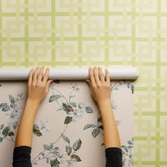 A pair of hands are shown reaching up to put new wall-paper over an older pattern.