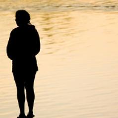 A woman stands silhouetted in front of rippling water.
