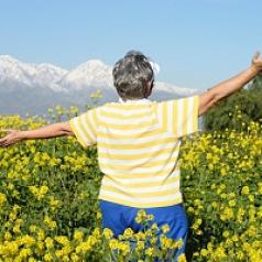 Older woman stands with amrs outstretched in field of wild flowers
