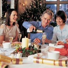 A man, surrounded by family, pours champagne at a holiday dinner.