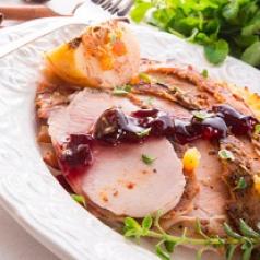 Cranberry sauce streaks slices of roasted turkey on a plate.