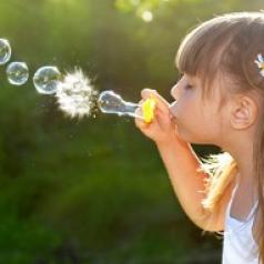 A small girl blows soap bubbles.