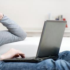 A man sits on a couch with a laptop on his lap.