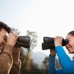 Young Asian couple in a forest smiling and  looking at each other through binoculars