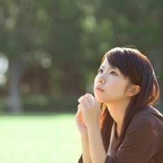 A young woman looks like she is thinking, while sitting outside.