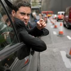 An angry man leans out of his car window and points his finger at someone.