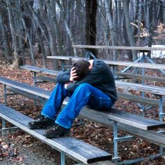 A boy sits on bleachers with his head on his knees