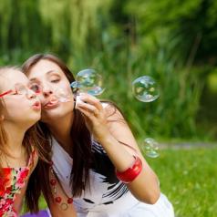Mother and little girl blowing bubbles in park