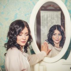 Woman looks away from mirror, downcast, while her reflection smiles
