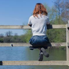Rear view of woman sitting on fence overlooking lake