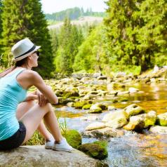 Woman in athletic clothes sits on rock and looks out at pond