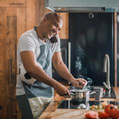 Man talking on the phone while cooking on a stove and holding a soccer ball