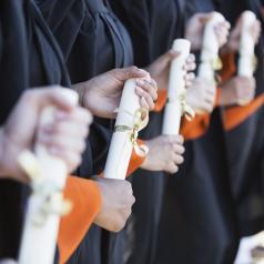 Closeup on the hands of a line of graduates who are holding their diplomas