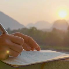 Closeup of hand writing in a journal in a pretty outdoor setting at sunrise