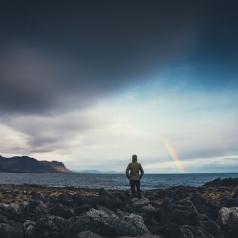 Person watching a rainbow in a cloudy sky