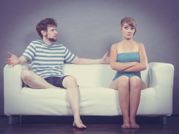 A young man holds open his arms for an embrace but his female partner looks distant