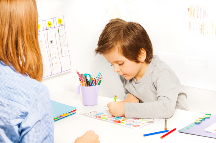 Boy colors in ABA session while therapist watches