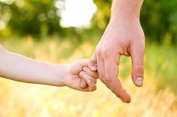 A child's hand clasps finger of parent
