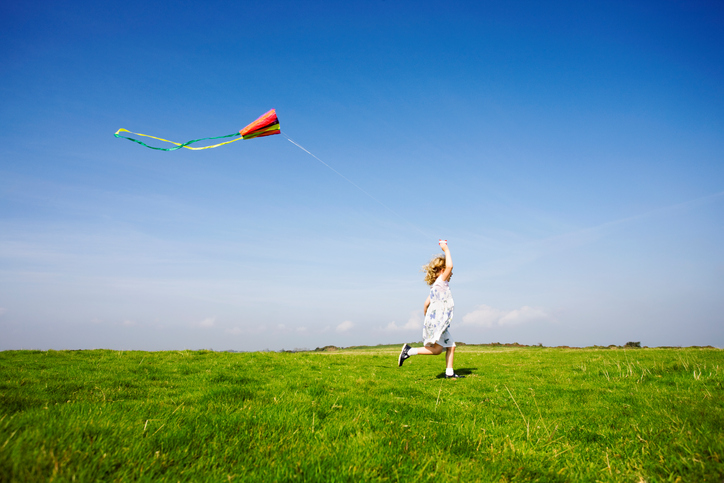 Young child with kite runs across green grass with blue sky beyond