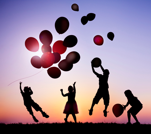 Children in shadow playing outdoors with balloons at sunset