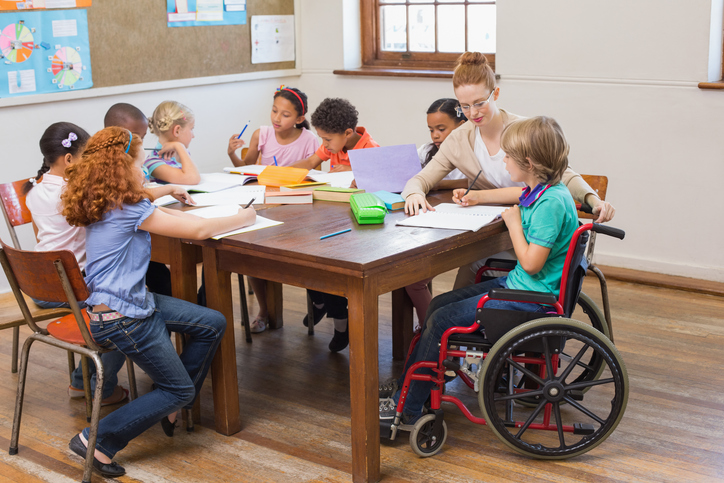 A group of children drawing and coloring at table with teacher in classroom