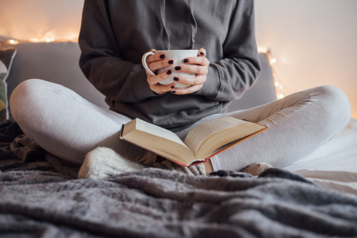 Cropped photo of woman reading and drinking tea in bed