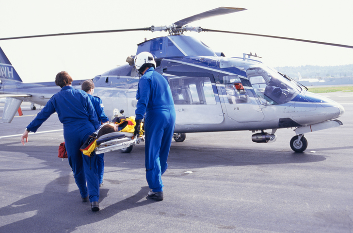 Three emergency personnel in blue uniforms carry person on stretcher to helicopter