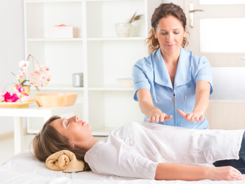 Female energy healer passes hands over body of woman receiving treatment