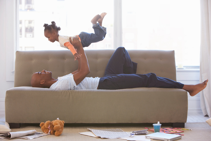 Father lying on sofa lifts daughter into the air