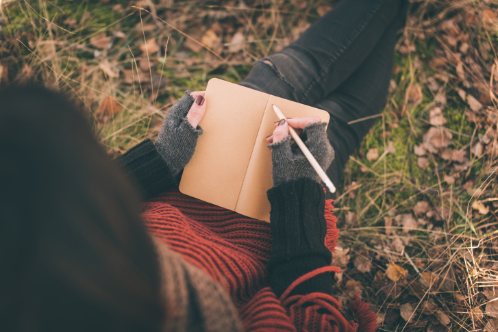 Girl sitting on grass writes in diary