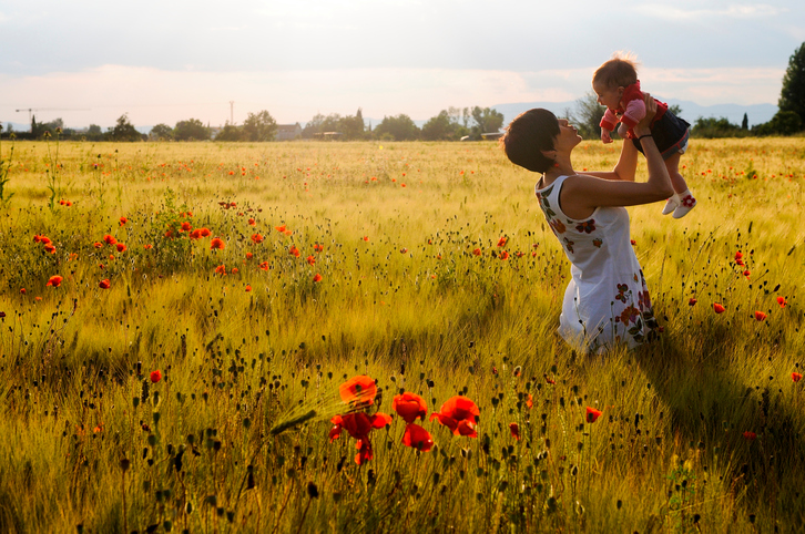 A smiling mother lifts up a baby in a field of poppies