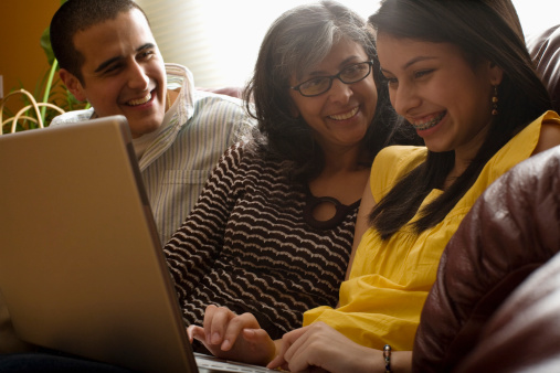 A teenager sits on sofa with parents and shows them how to use a laptop