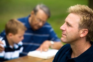 Un homme pensif regarde au loin, avec son père et son fils en arrière-plan.