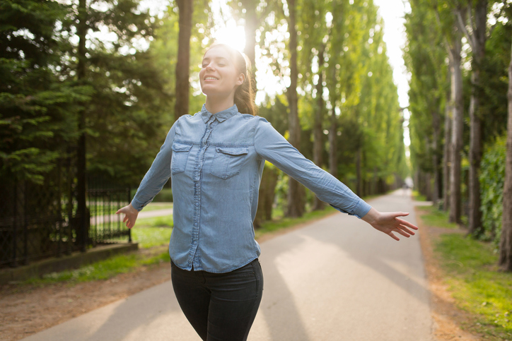 Person walking on tree-lined path stretches arms and smiles