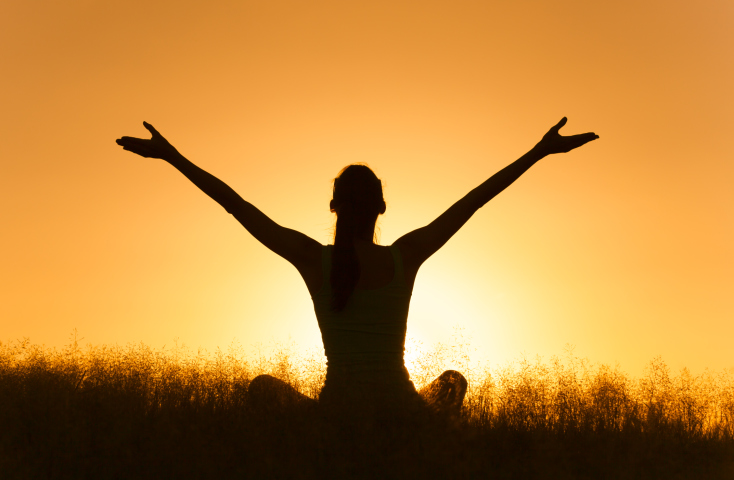 Person raises arms to sky against a sunset