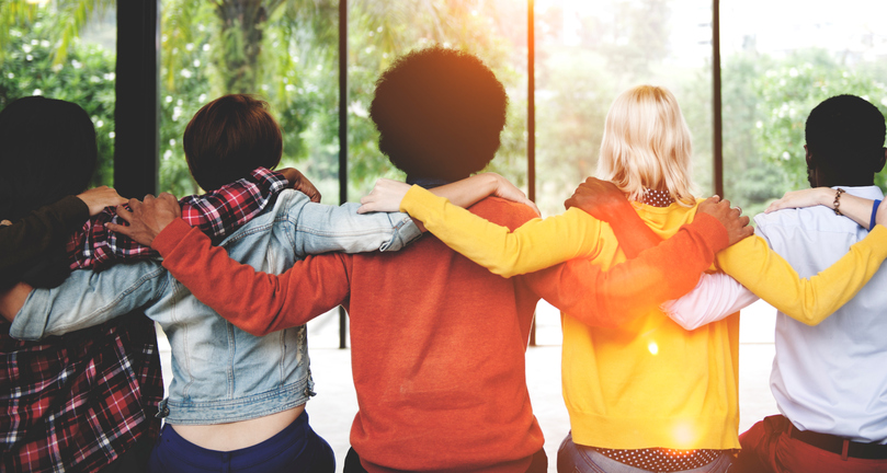 A group of friends faces away from the camera, arms thrown over each others' shoulders