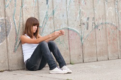 Young woman sits on sidewalk, leaning against a wall of graffiti.