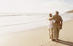 A senior couple walks the beach with arms around each other