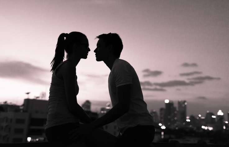 Grayscale photo of shadowed couple kissing at sunset