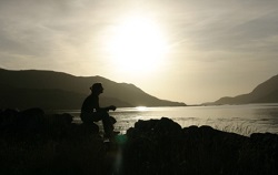 Silhouette of a person seated on a rock, contemplating a beautiful landscape