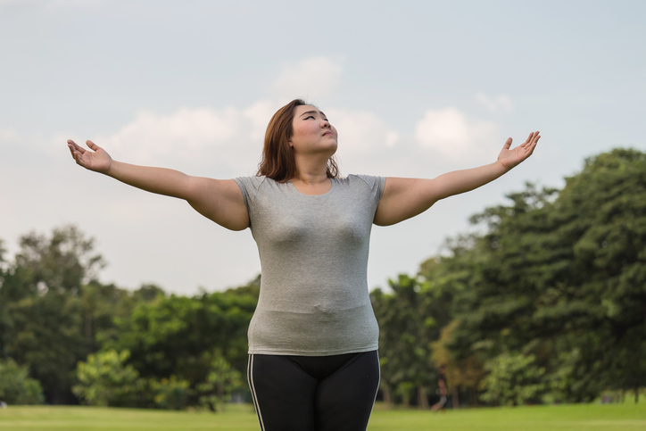 Woman stretches out arms to do deep breathing exercise in grassy space with trees