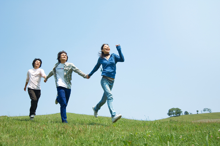 Three young adults run across field with hands linked