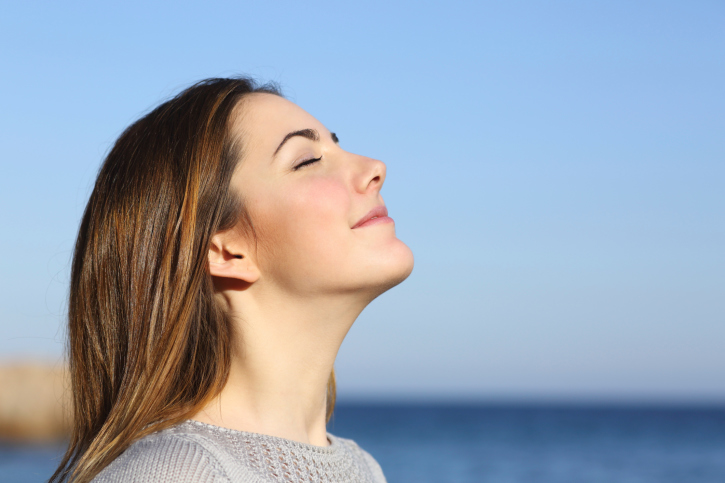 Woman standing beside ocean, breathing in deeply