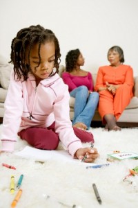 Girl sitting on floor coloring with mother in background