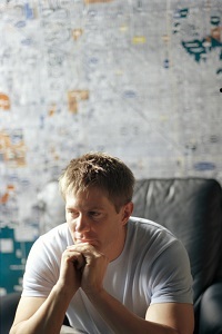 A man sits in a chair with his chin propped on his hand and thinks.
